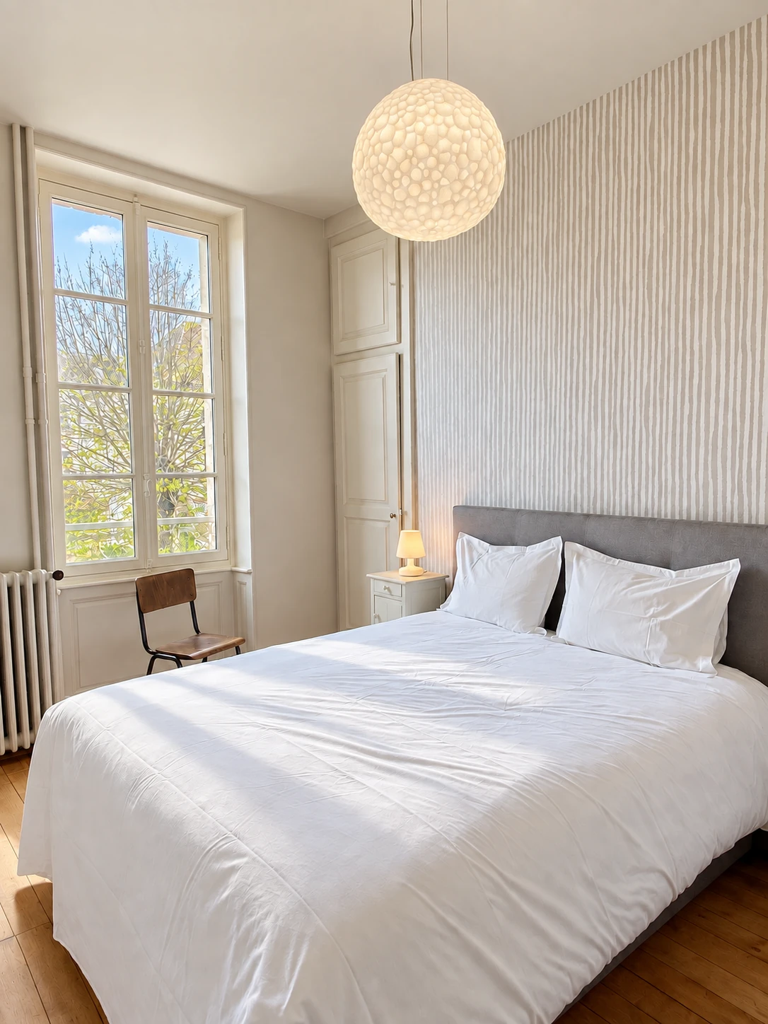 Das Doppelbett vom Fuß bis zum Boden, vor der gestreiften Wand und dem großen Fenster
