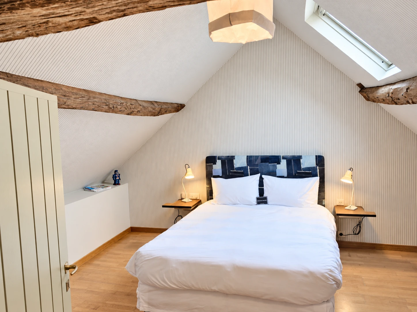 La chambre mansardée de l’appartement n°6, son lit double et ses poutres apparentes